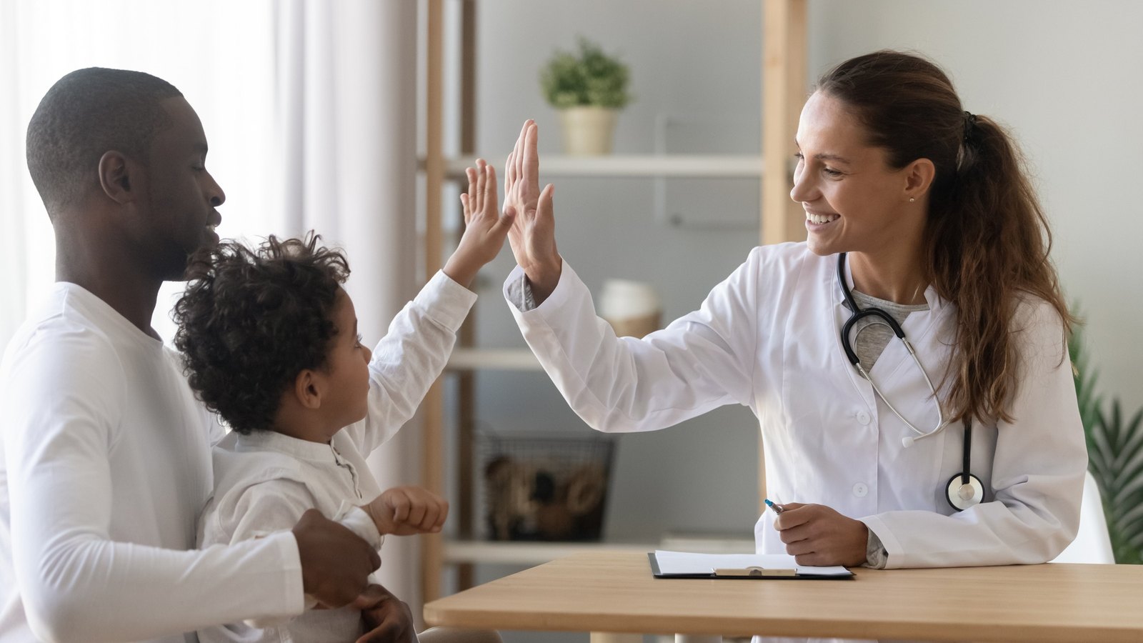 Doctor giving a young patient a high five while his father holds him