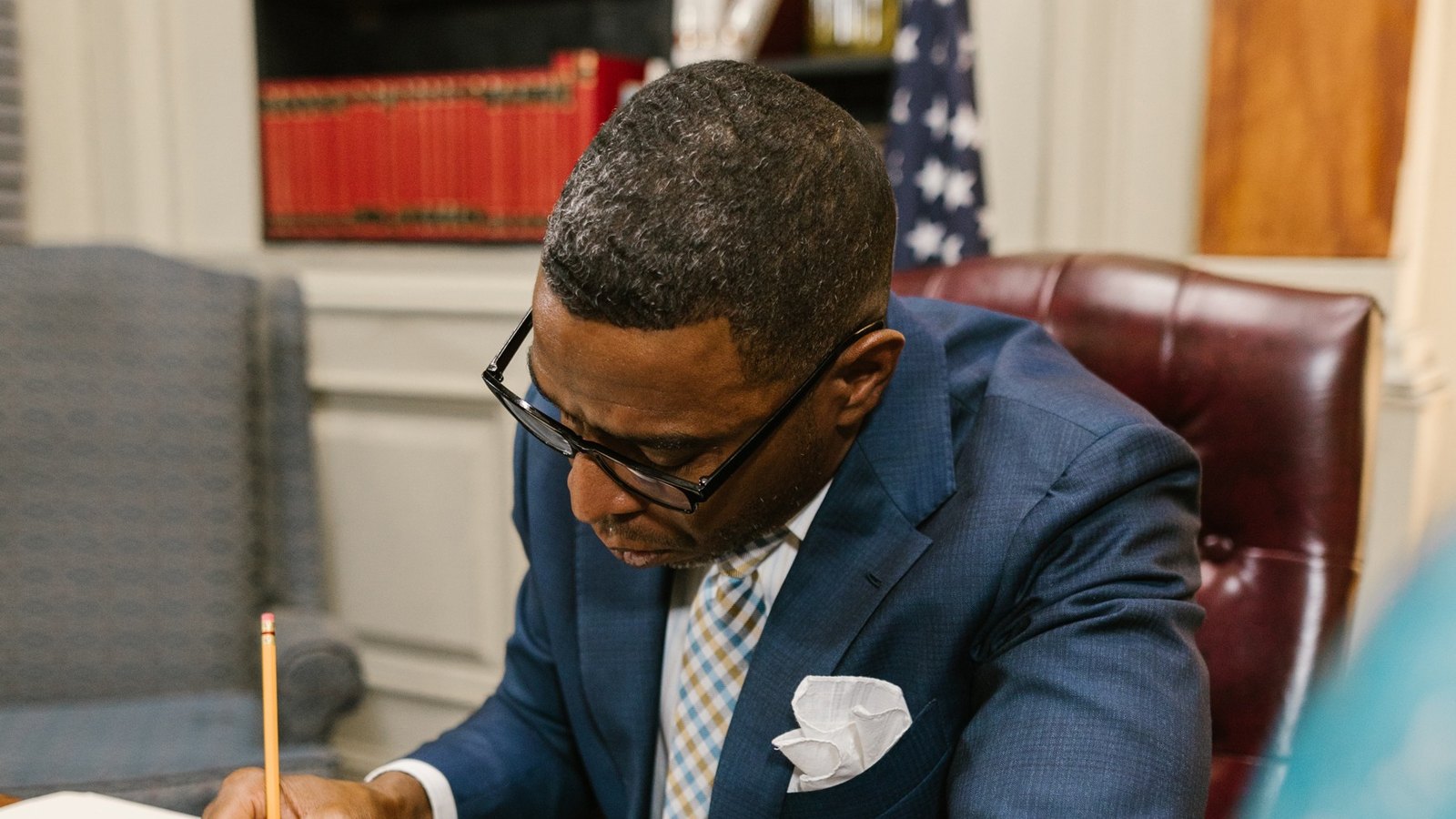 Attorney at his desk reviewing a document, law books and a flag behind him