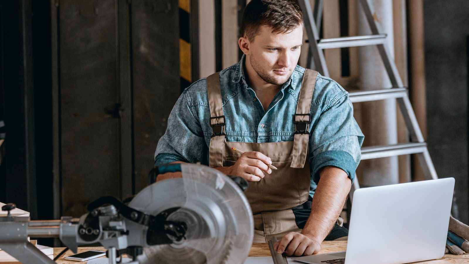 Contractor at his workshop bench checking a search result on his laptop